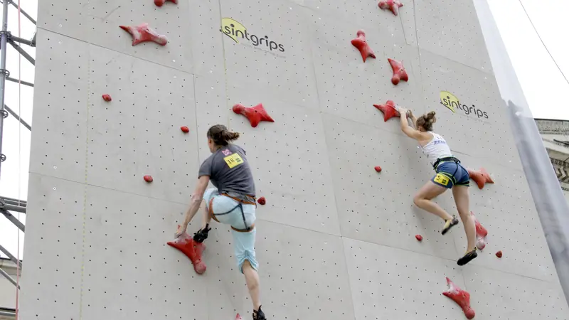 Two climbers racing side by side up an outdoor speed wall with red holds